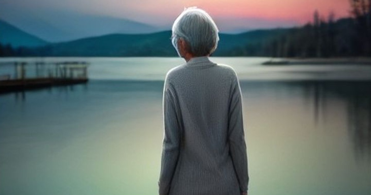 A woman stands alone at the end of a lakeside dock at dawn, looking out over still water.
